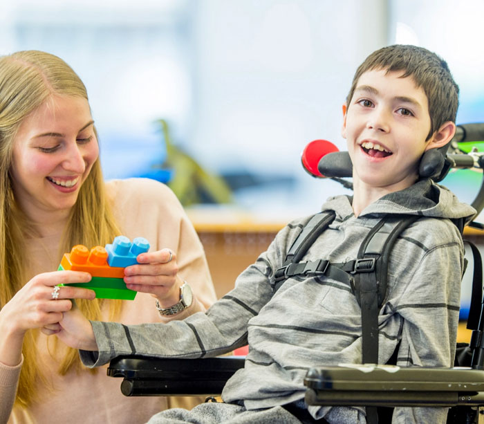 Caregiver assisting a child in a wheelchair with building blocks, both smiling and enjoying the activity.