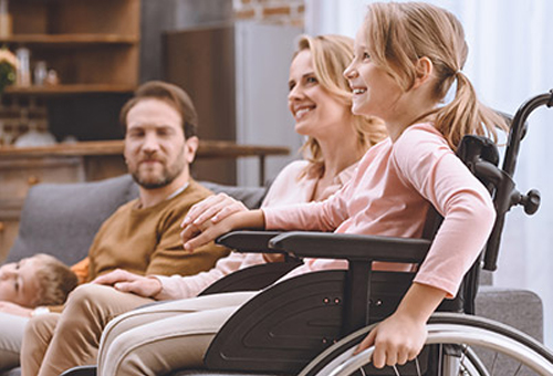 A family sitting together on the couch, with a young girl in a wheelchair, highlighting family support and care in a comfortable home environment.