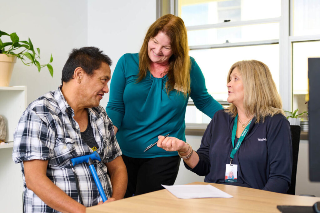 A person receiving in-home support during a consultation with two support workers, focusing on communication, care, and assistance in a comfortable setting.