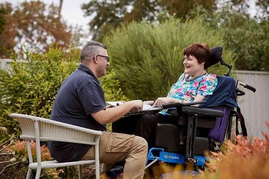 A caregiver assisting a person in a wheelchair in a garden setting, offering support and companionship in a peaceful outdoor environment.