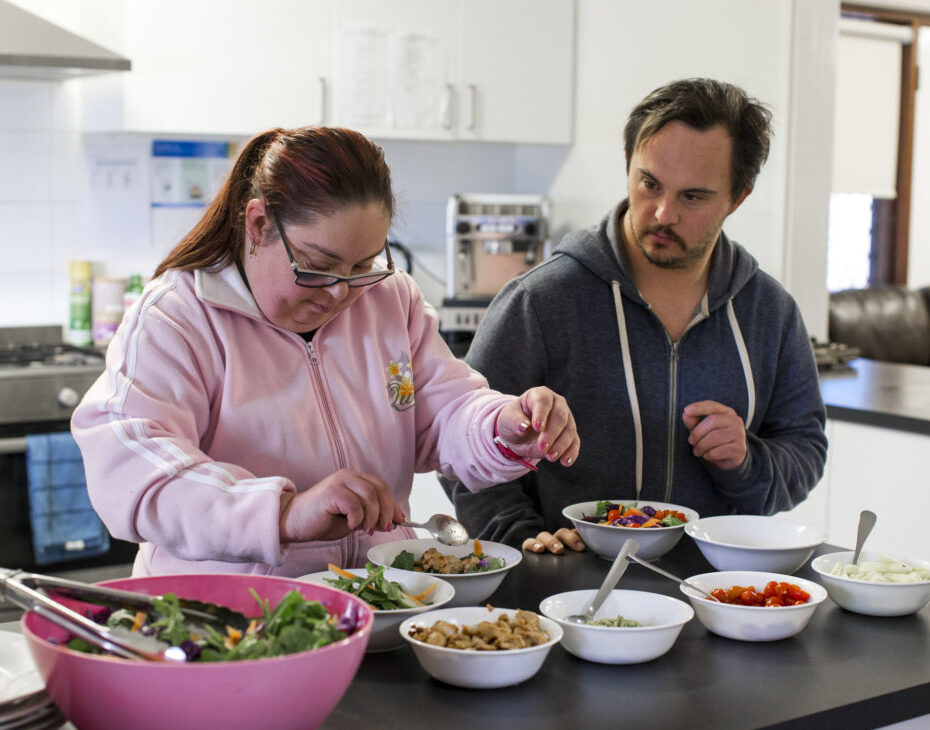 A caregiver and a participant preparing a meal together in the kitchen, focusing on meal preparation and developing daily living skills.